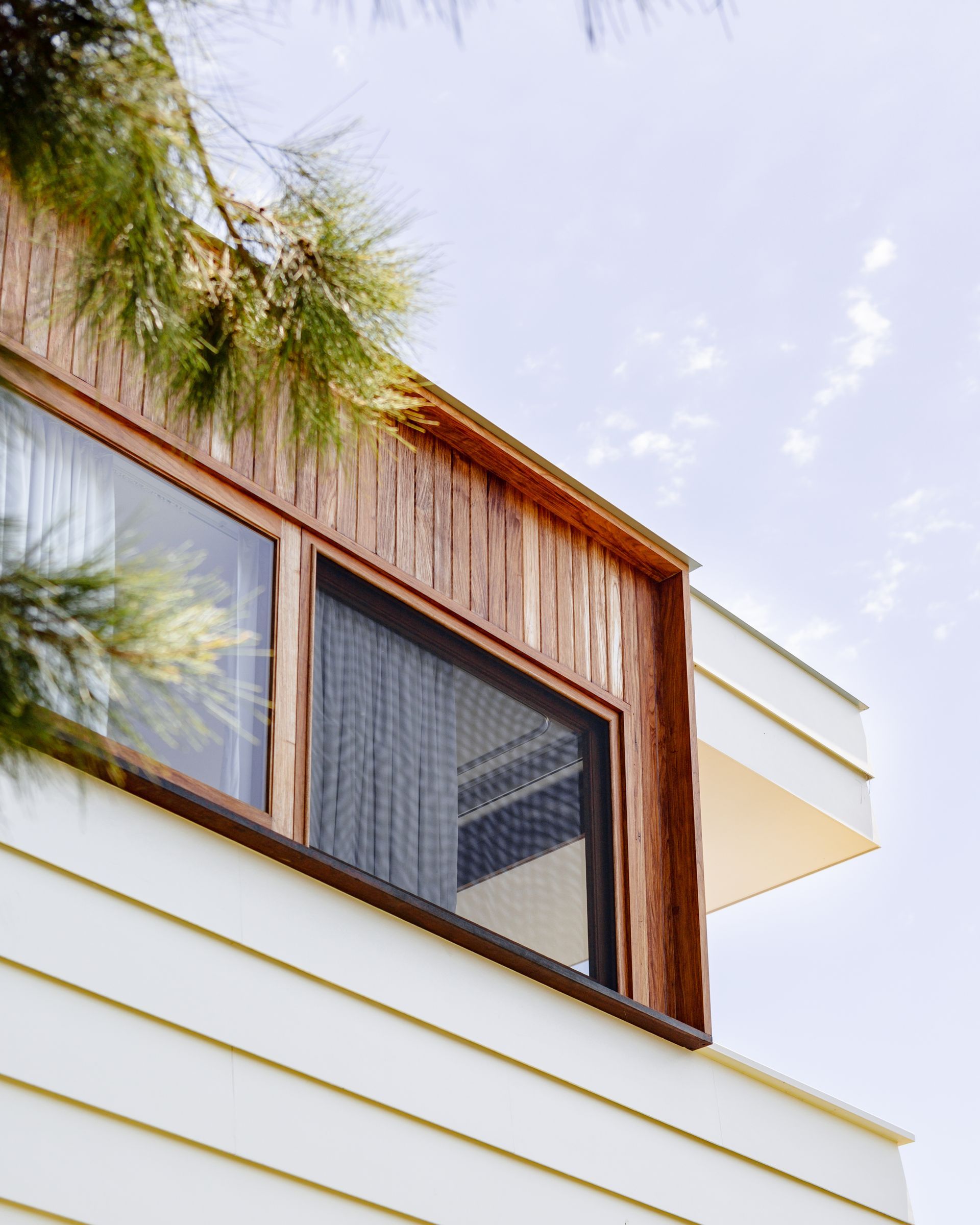 Close-up of a modern building with horizontal white siding, wooden trim, and a large window.
