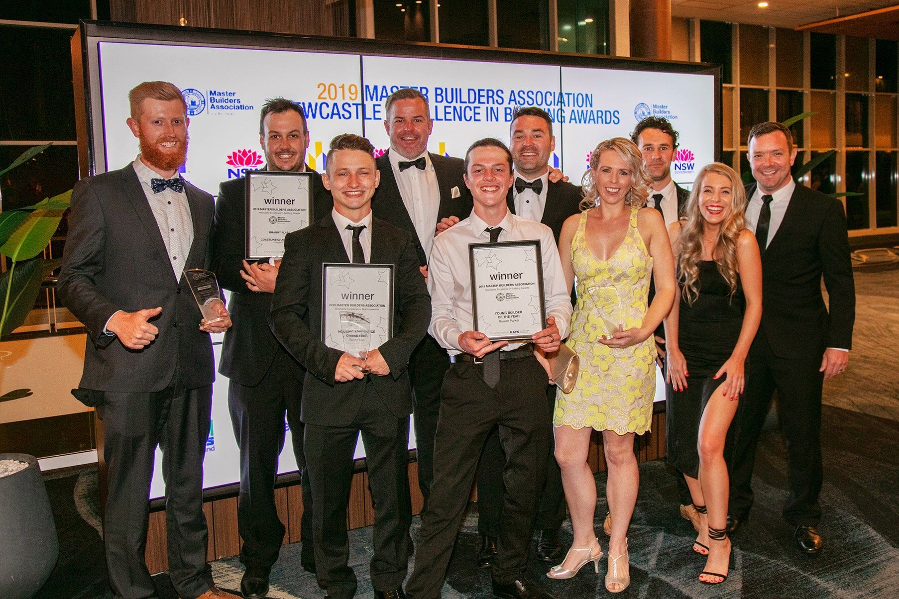 Group of people holding awards at an event, likely an awards ceremony, in front of a backdrop.