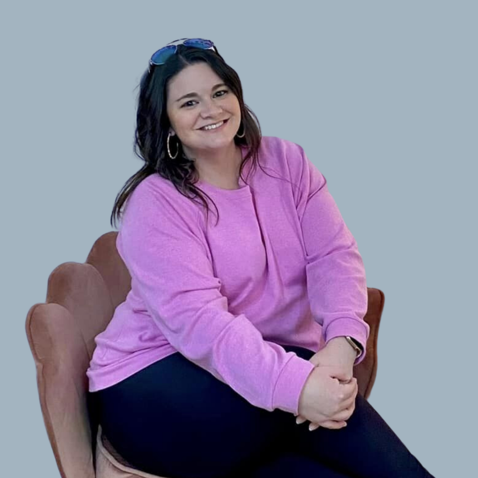 a woman in a purple sweater is sitting in a chair with her hands folded .