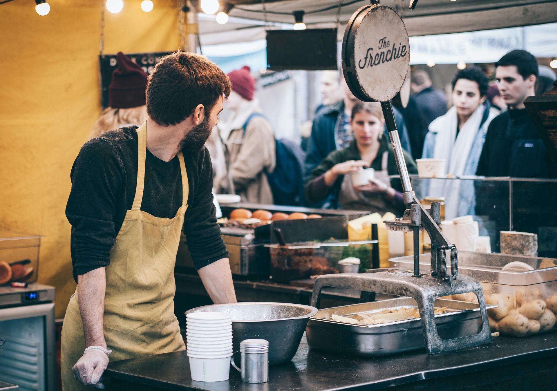 A man in a yellow apron is standing at a food stand.