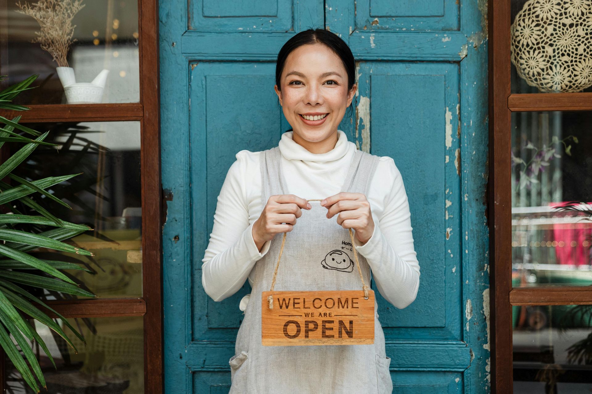 A woman is holding a welcome open sign in front of a blue door.