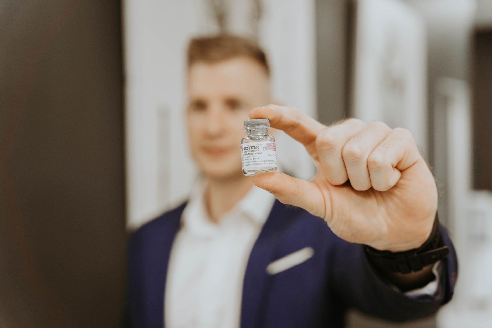 A man in a suit is holding a small bottle of vaccine in his hand.