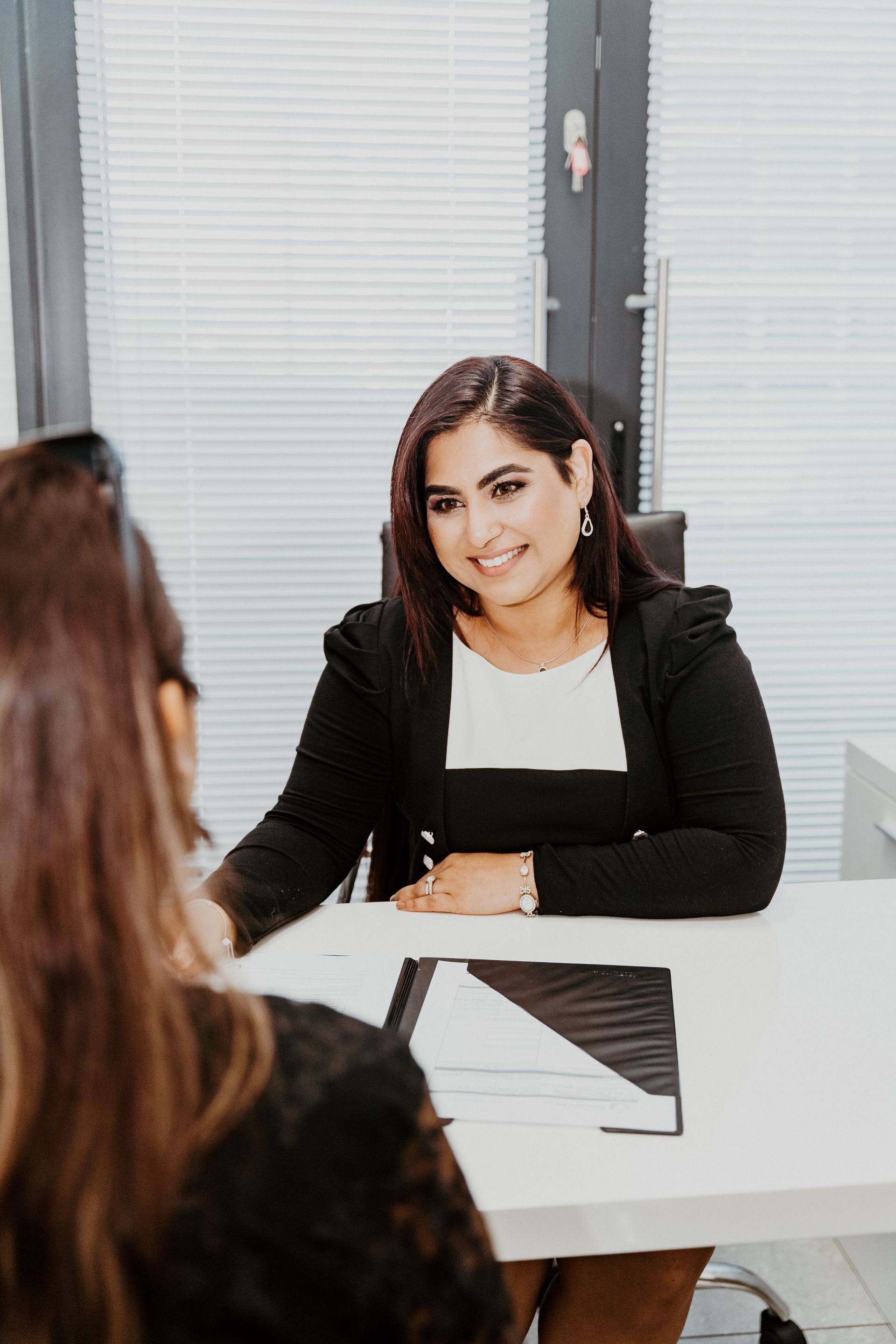 A woman is sitting at a desk talking to another woman.