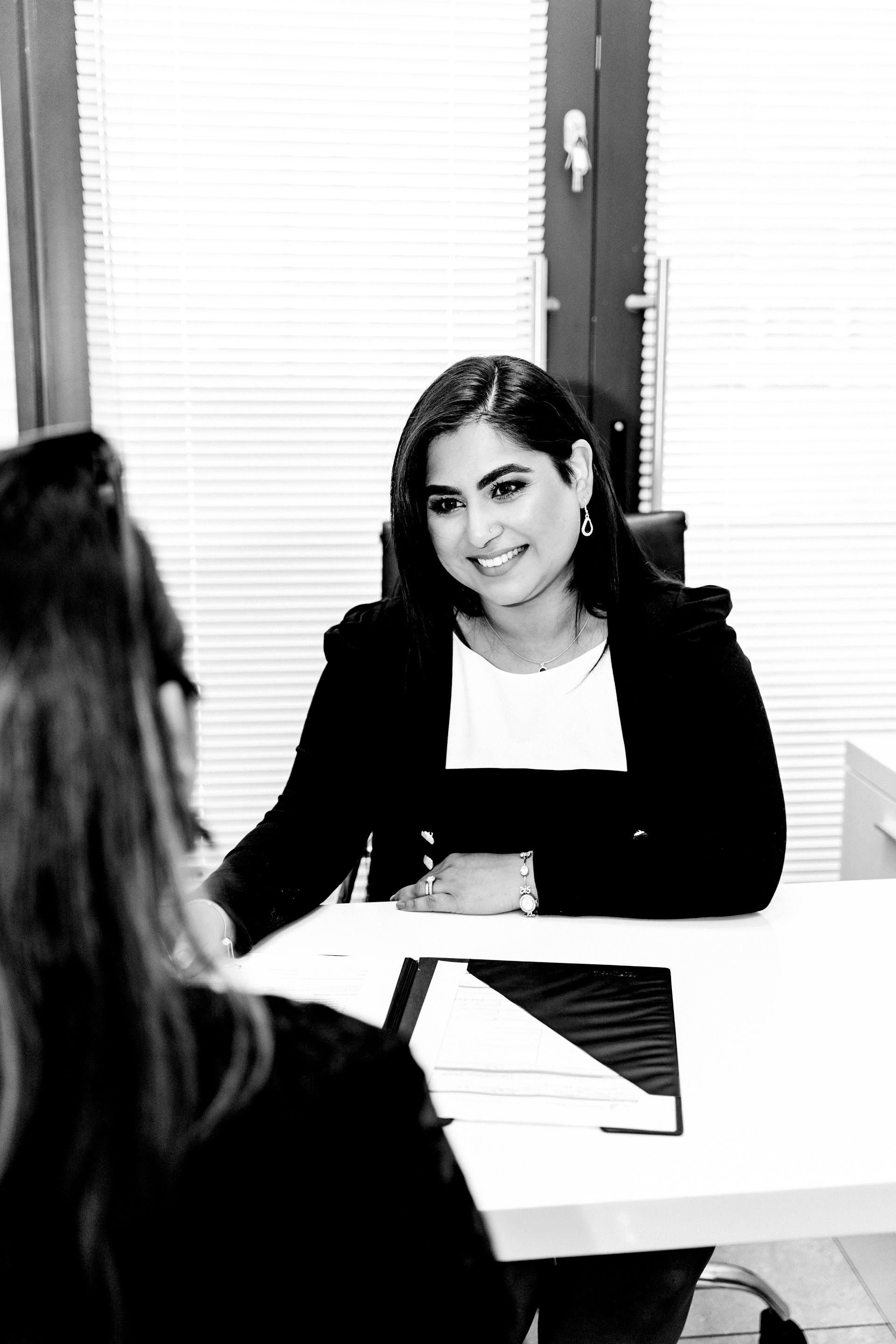 A woman is sitting at a desk talking to another woman.