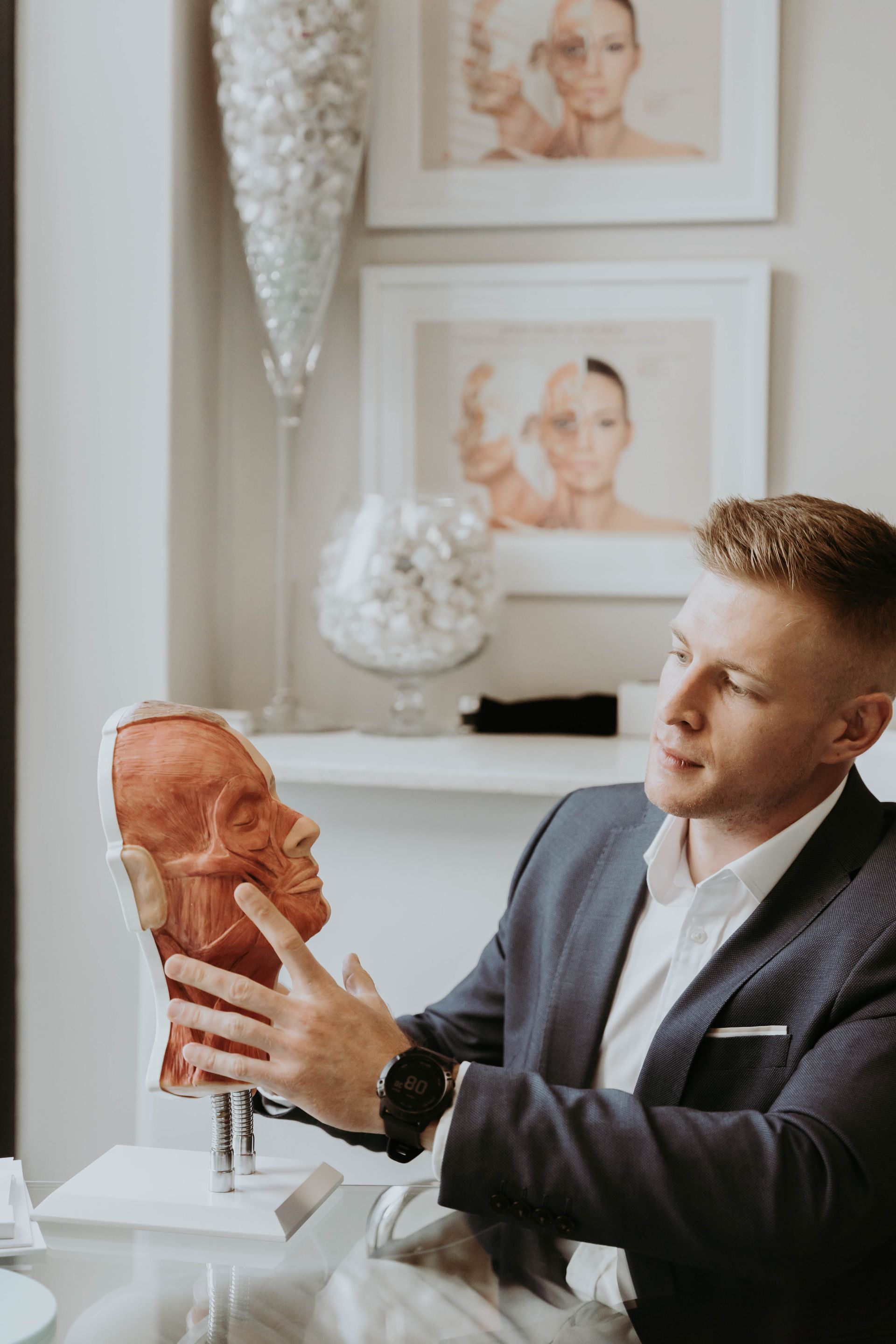 A man in a suit is sitting at a table holding a model of a face.
