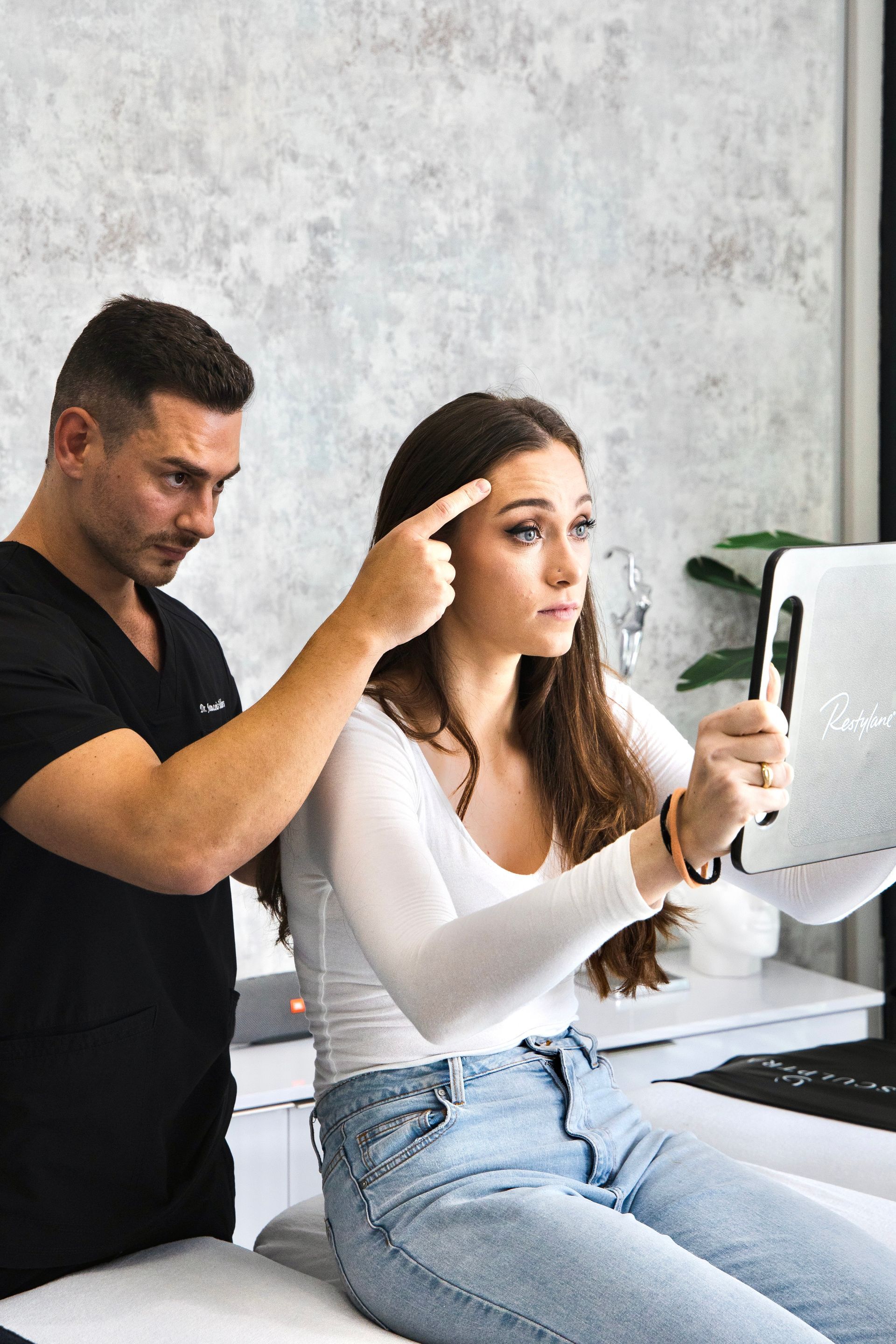 A man is pointing at a woman 's face while she looks at a tablet.