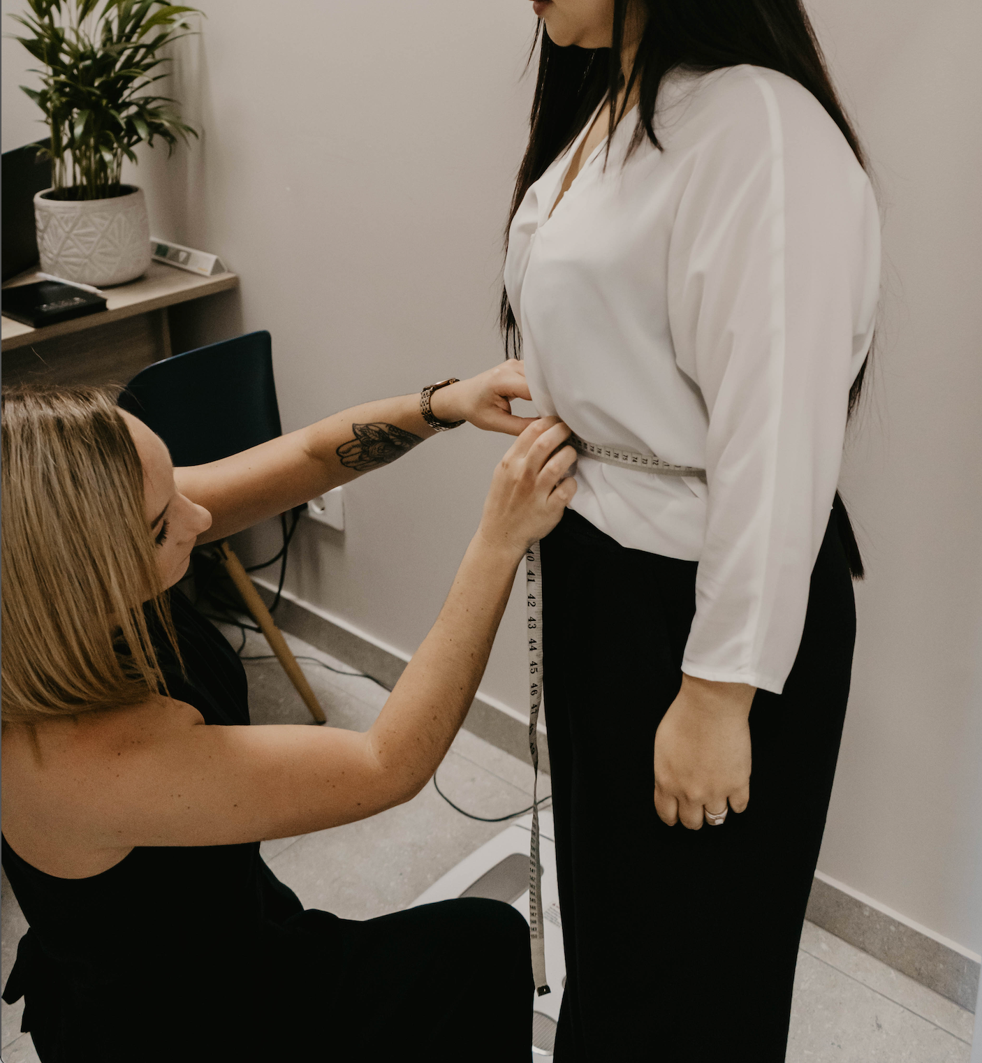 A woman is measuring another woman 's waist with a tape measure