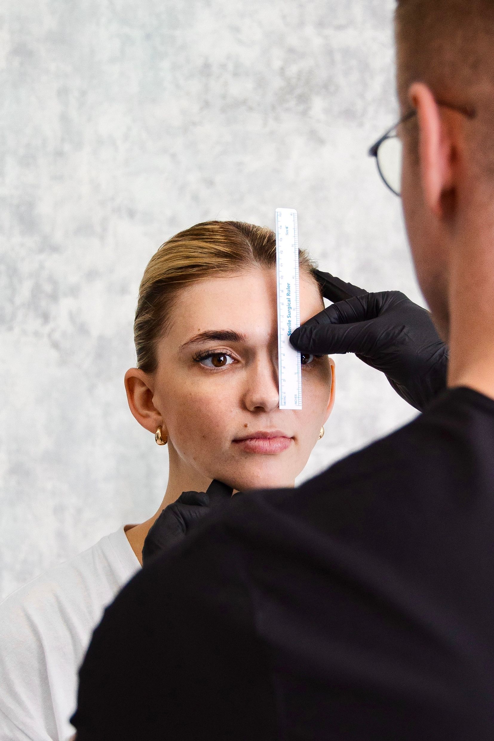 A man is measuring a woman 's eyebrows with a ruler.
