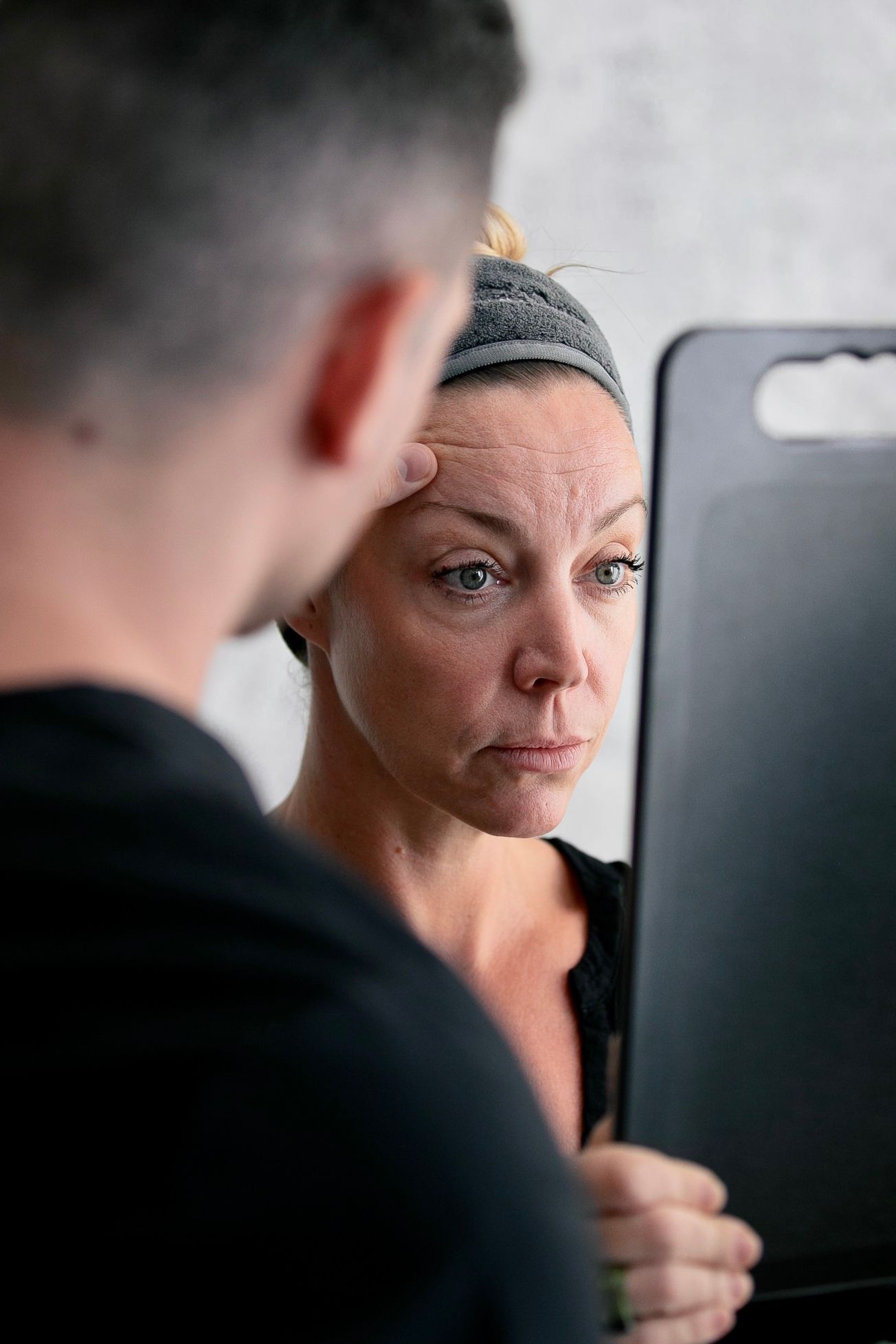 A man is looking at a woman 's face in a mirror.