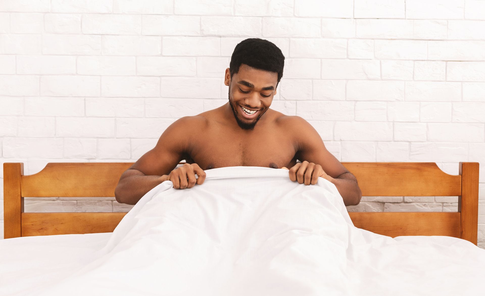 A shirtless man is laying in bed under a blanket.