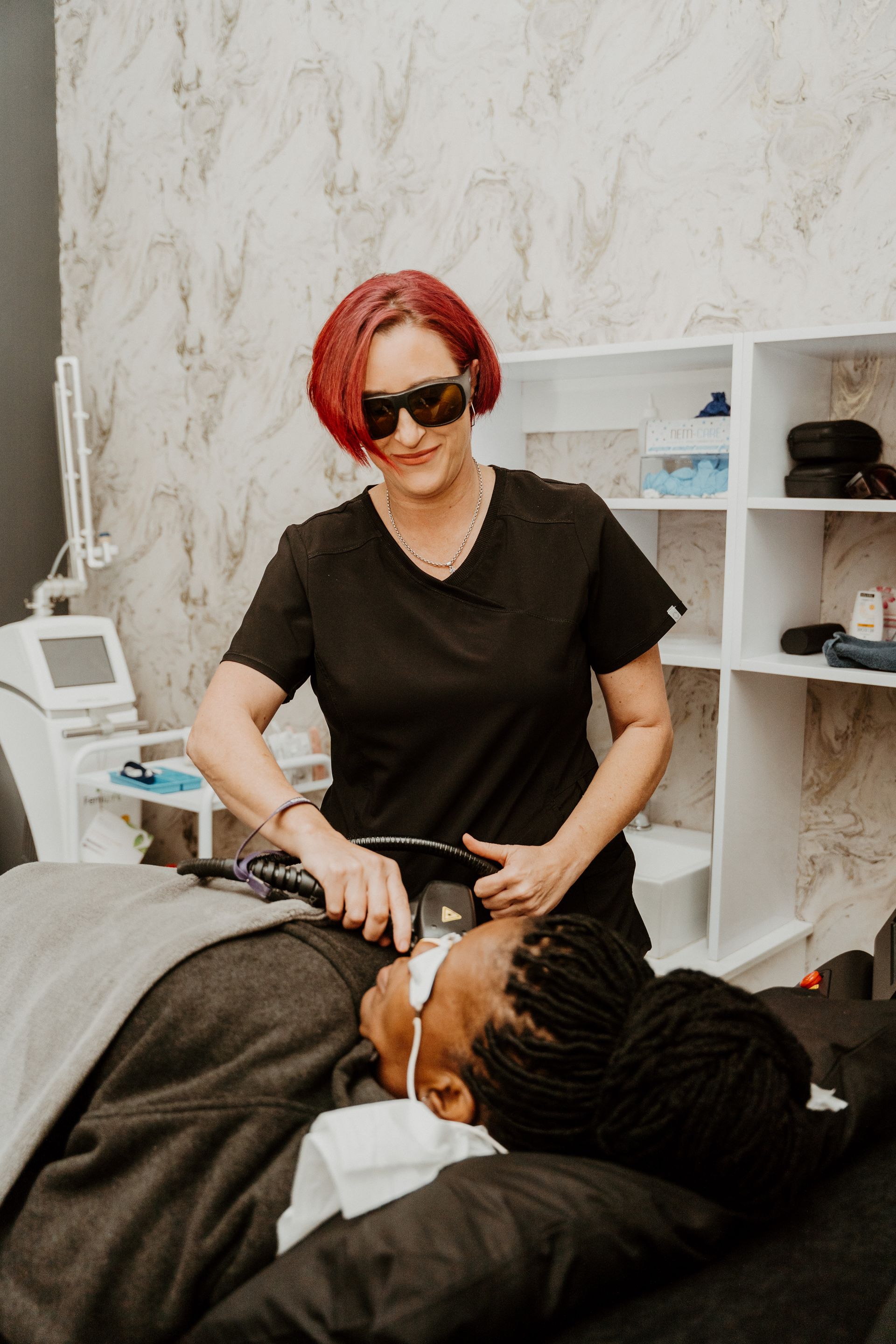 A woman is standing next to a man laying on a bed.