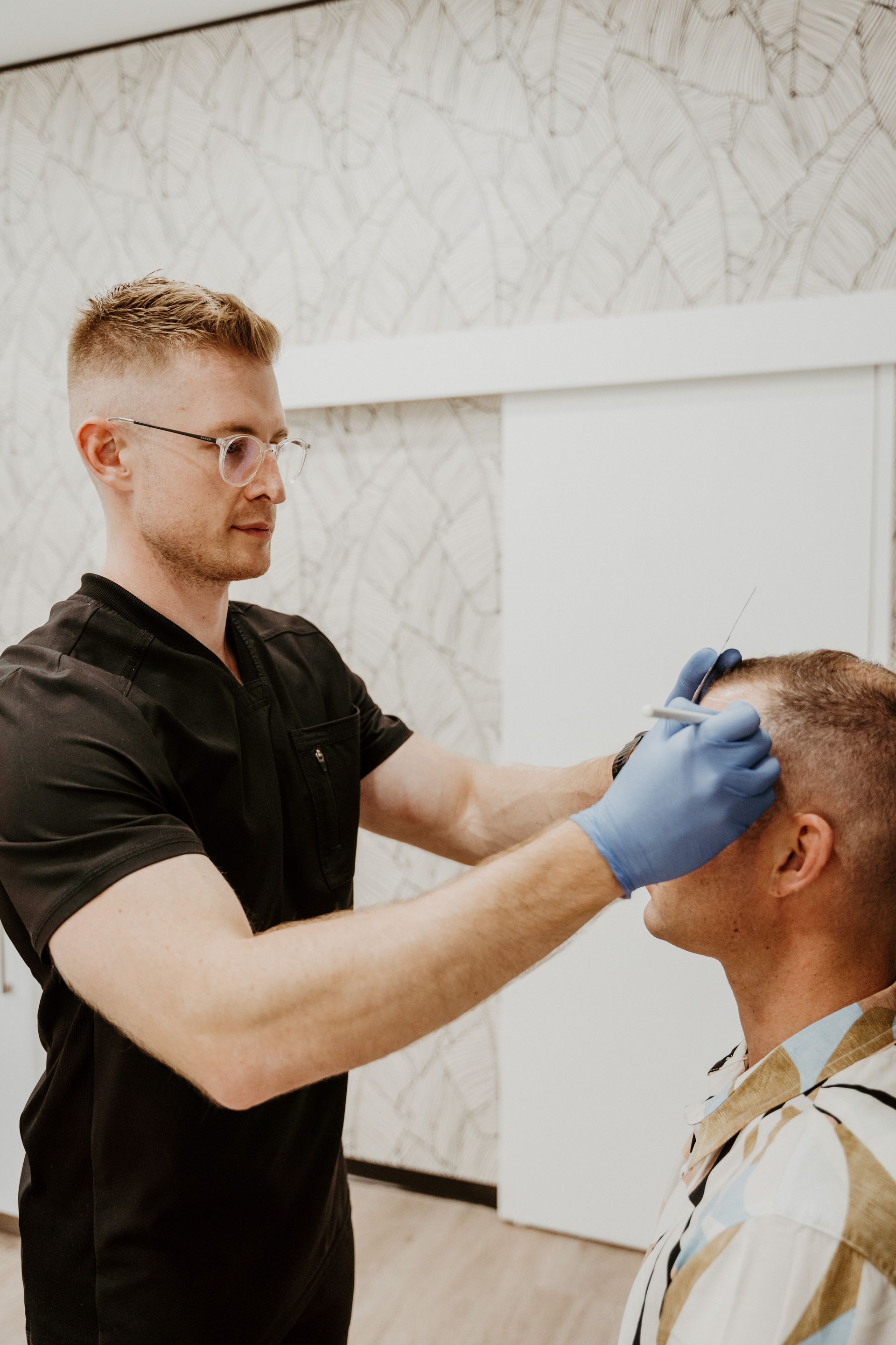 A man in a black shirt and blue gloves is examining another man 's eye.