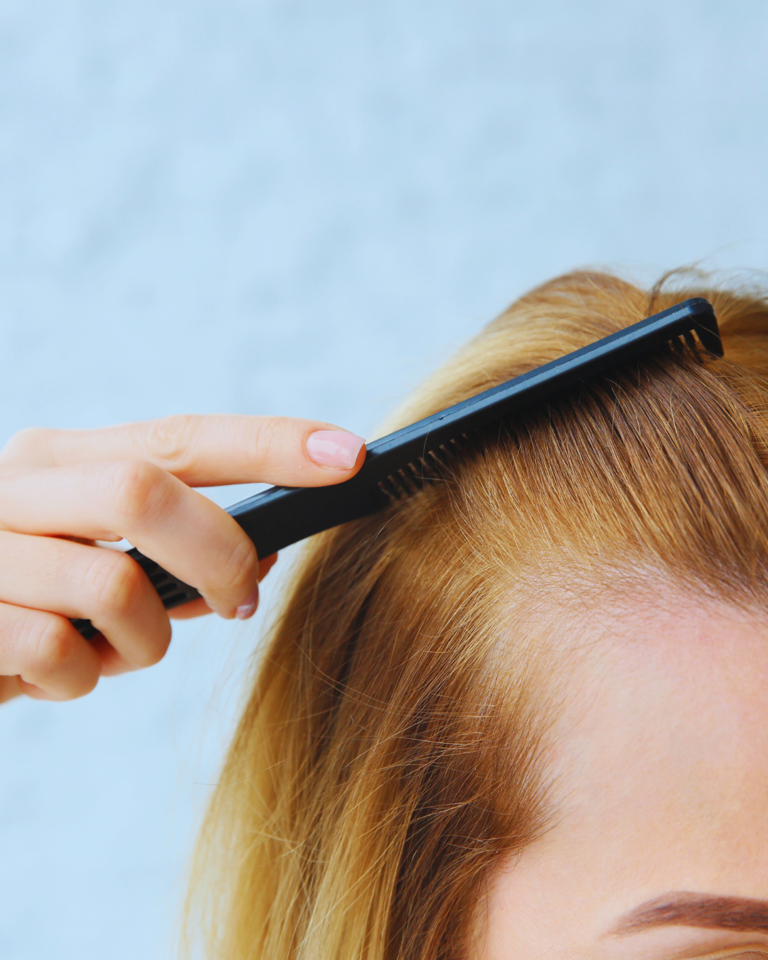 A woman is brushing her hair with a black comb.