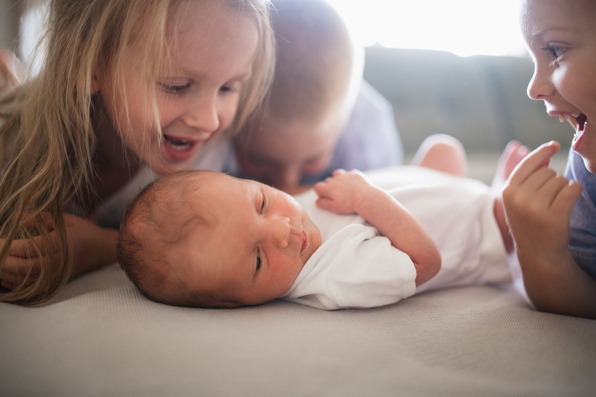 Three children are looking at a newborn baby laying on a bed.