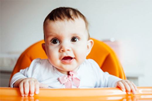 A baby is sitting in an orange high chair and smiling.