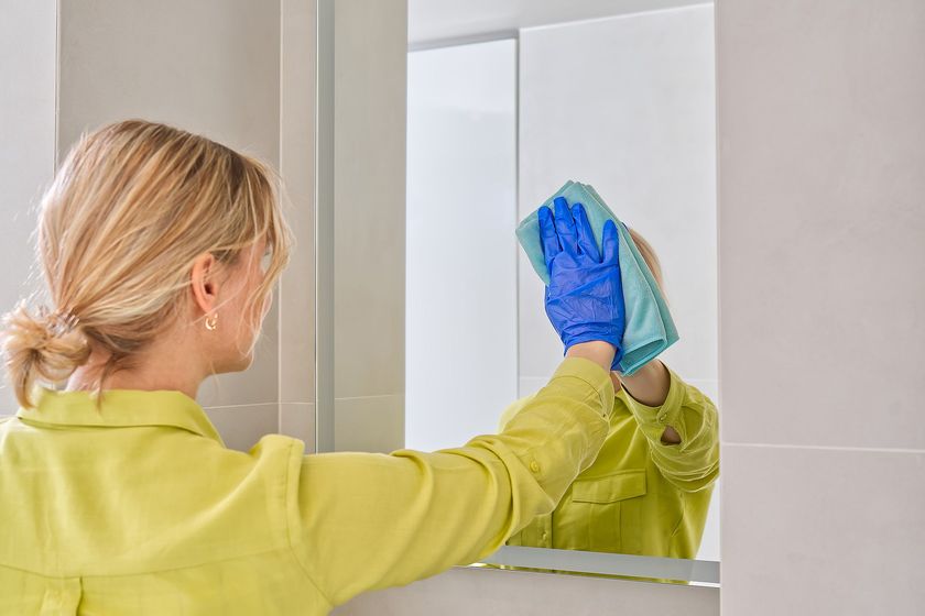 a woman cleaning a mirror with a blue glove