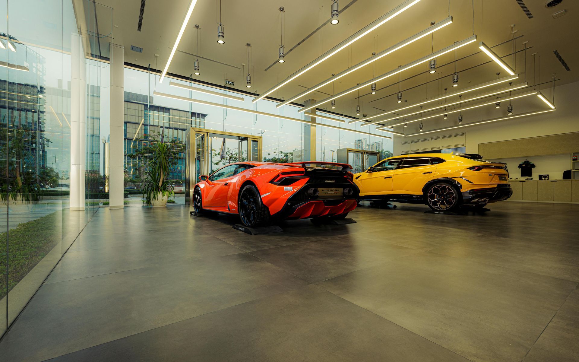 A bright, modern showroom featuring a red sports car and a yellow SUV parked on a polished concrete floor.