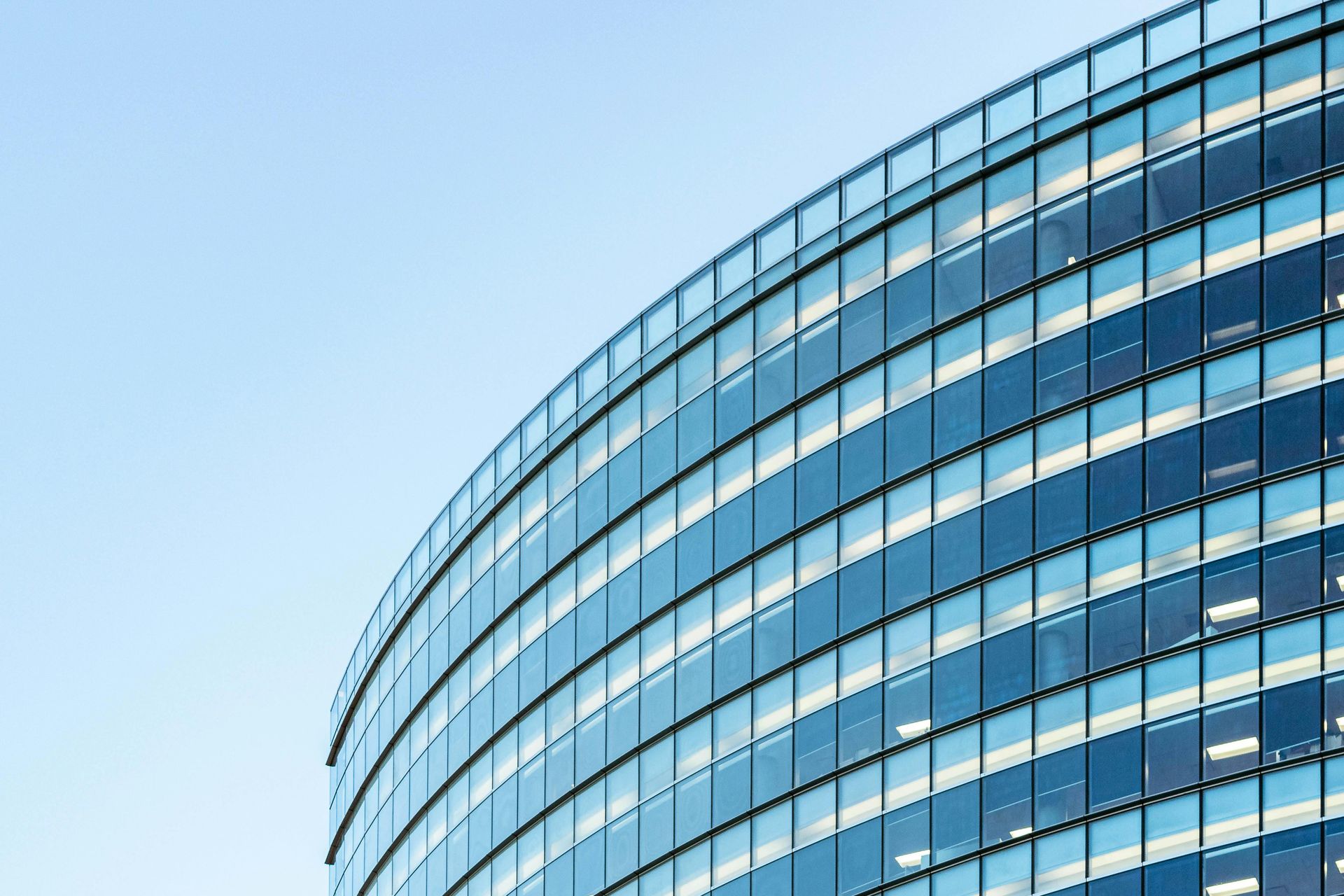 Curved glass office building exterior against a clear blue sky.