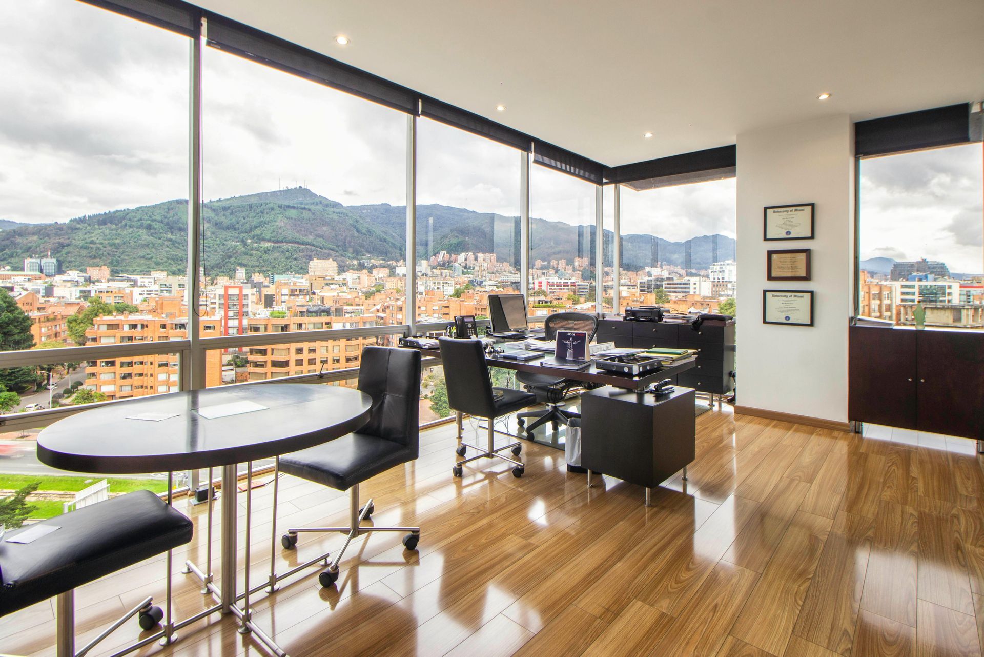 A modern, high-rise office with a polished wood floor, a desk, and a table overlooking a city and mountain landscape with our professional office cleaning sydney