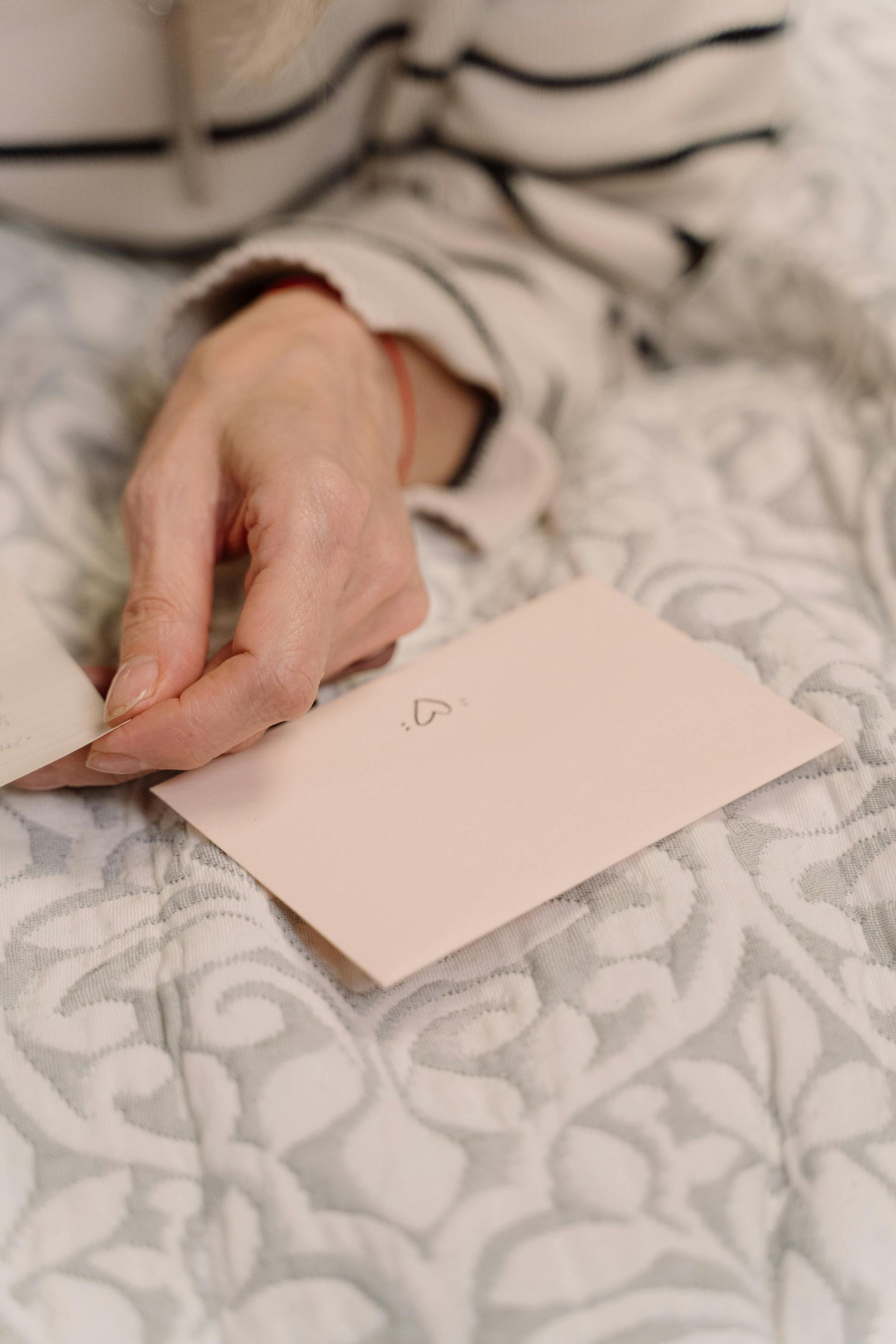 A person is laying on a bed holding a pink envelope.
