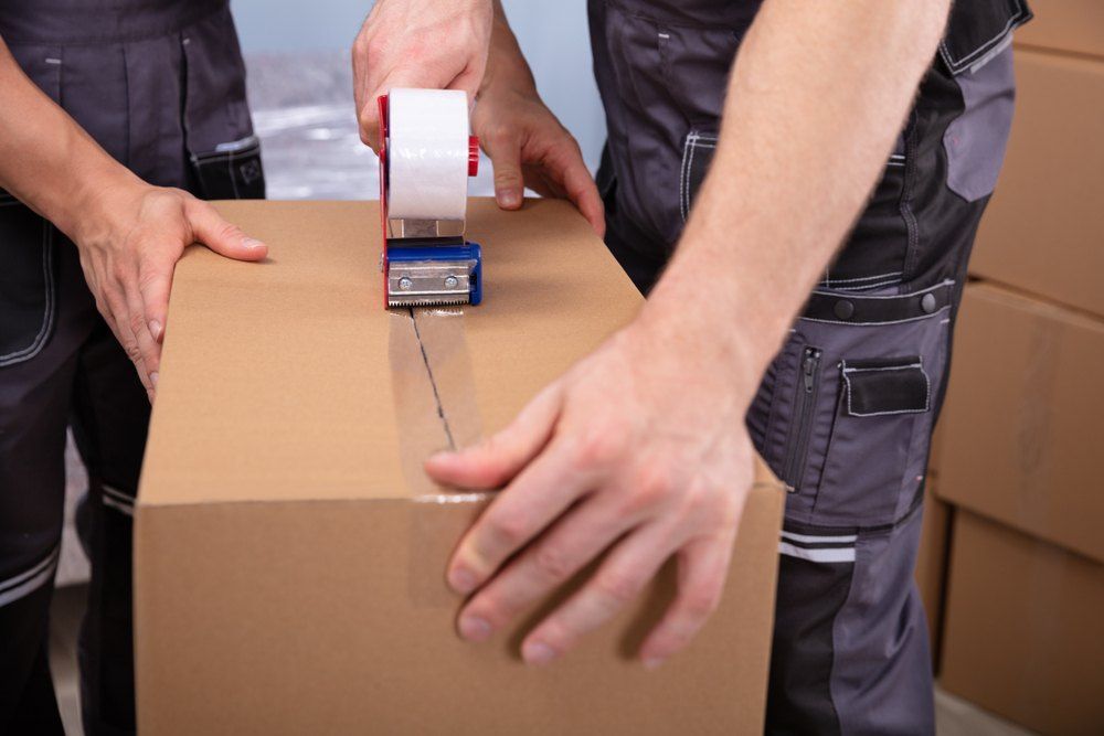 Two Men Are Taping a Cardboard Box With Tape — Buck Removals & Storage in Cowra, NSW