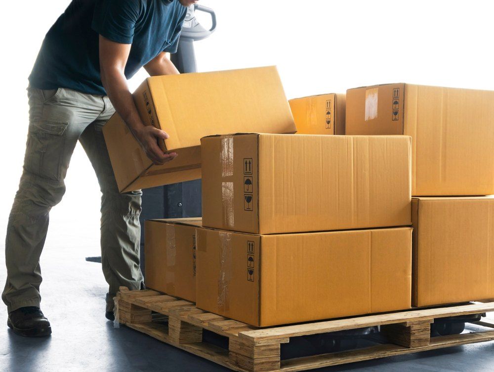 A Man is Loading Boxes Onto a Wooden Pallet — Buck Removals & Storage in Griffith, NSW