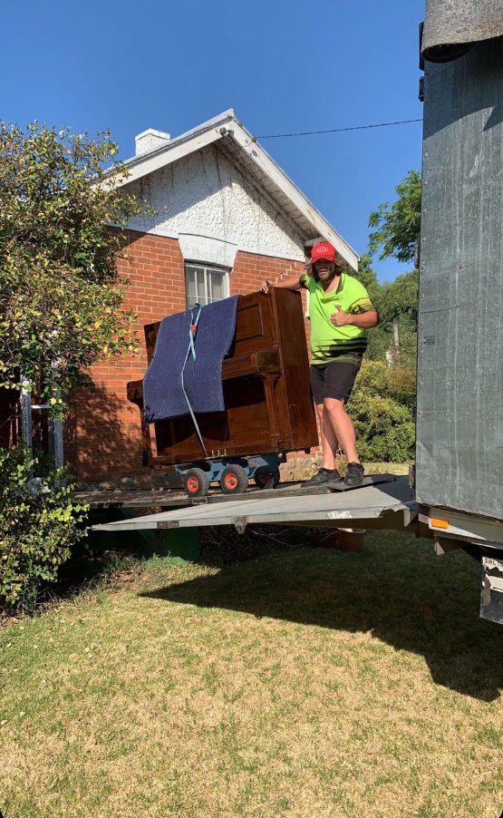 A Man is Carrying a Piano on the Back of a Truck — Buck Removals & Storage in Cowra, NSW
