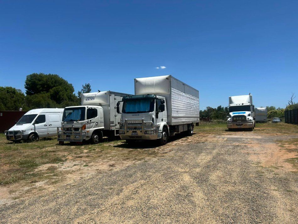 A Row of White Trucks Are Parked in a Dirt Lot — Buck Removals & Storage in Bathurst, NSW
