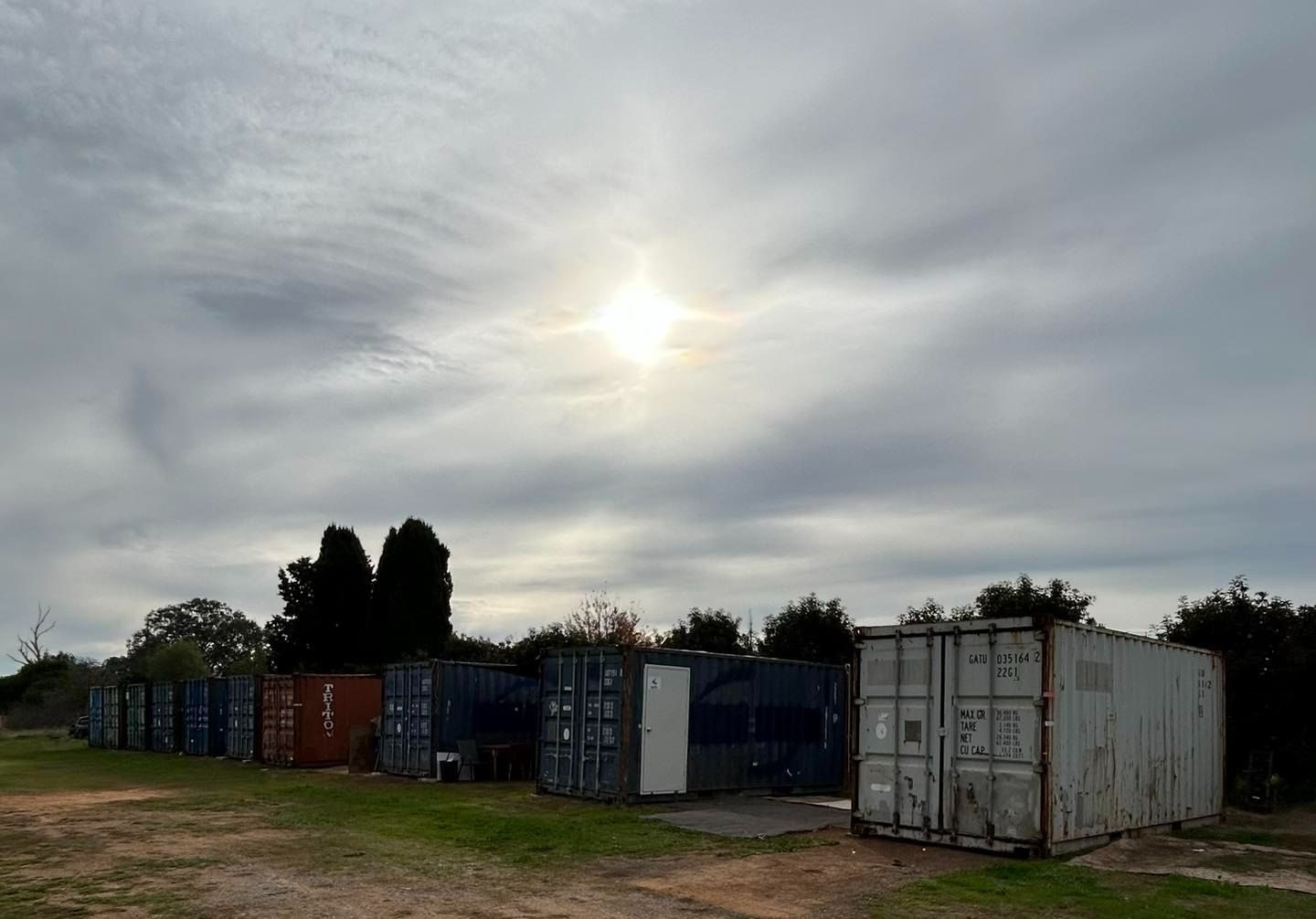 A Row of Shipping Containers in a Field With the Sun Shining Through the Clouds — Buck Removals & Storage in Bathurst, NSW