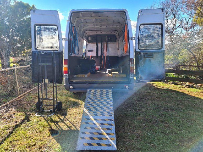 A Van With a Ramp Attached to the Back of It is Parked in a Grassy Field — Buck Removals & Storage in Parkes, NSW