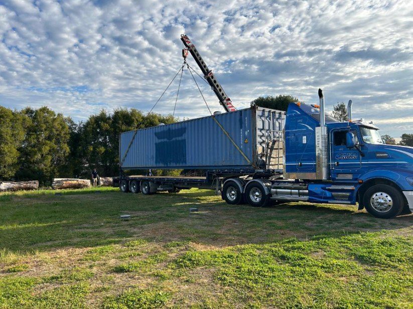 A Blue Semi Truck is Being Lifted by a Crane in a Grassy Field — Buck Removals & Storage in Cowra, NSW