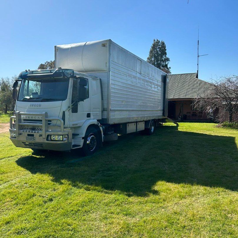 A White Truck is Parked in a Grassy Field in Front of a House — Buck Removals & Storage in Wagga Wagga, NSW