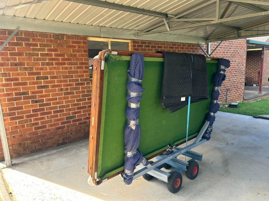 A Pool Table is on a Cart Under a Brick Building — Buck Removals & Storage in Parkes, NSW