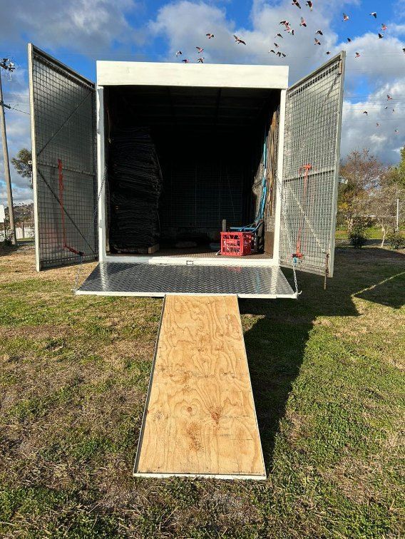 A Trailer is Sitting in the Grass With Its Doors Open — Buck Removals & Storage in Cowra, NSW