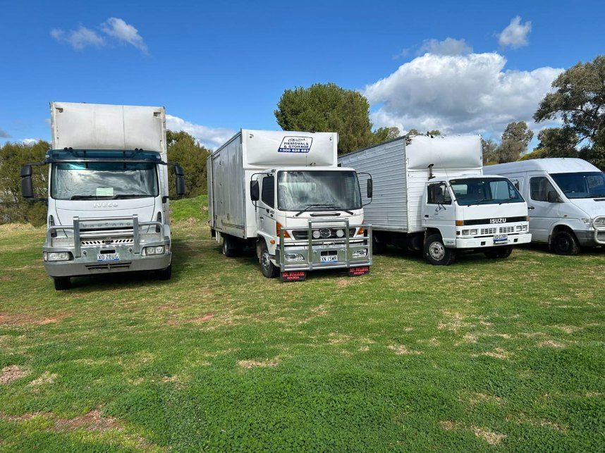 A Row of Moving Trucks Are Parked in a Grassy Field — Buck Removals & Storage in Young, NSW