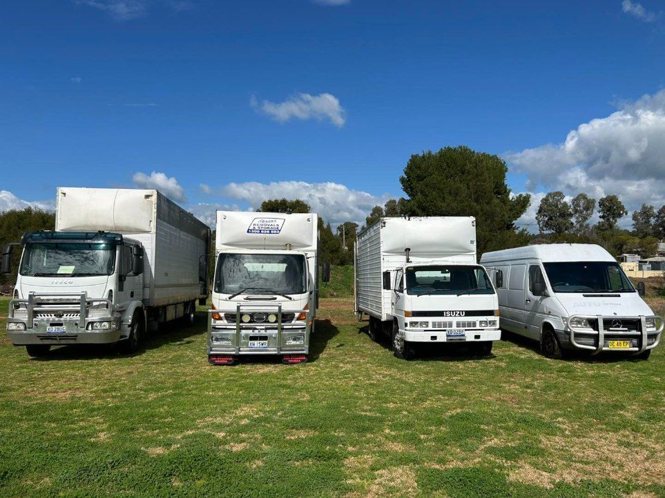 Four White Trucks and a White Van Are Parked in a Grassy Field — Buck Removals & Storage in Griffith, NSW