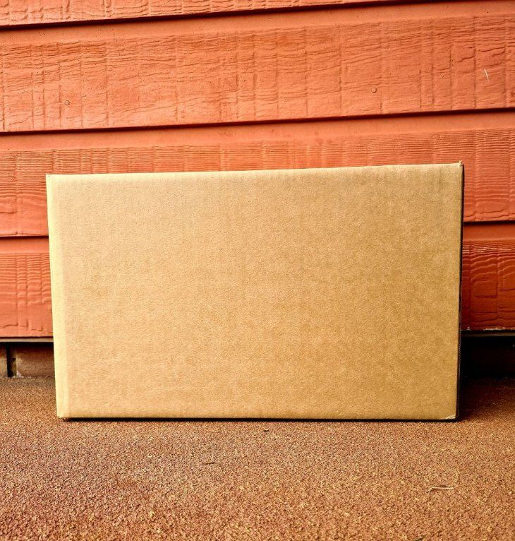 A Cardboard Box is Sitting on the Ground in Front of a Red Wall — Buck Removals & Storage in Cowra, NSW