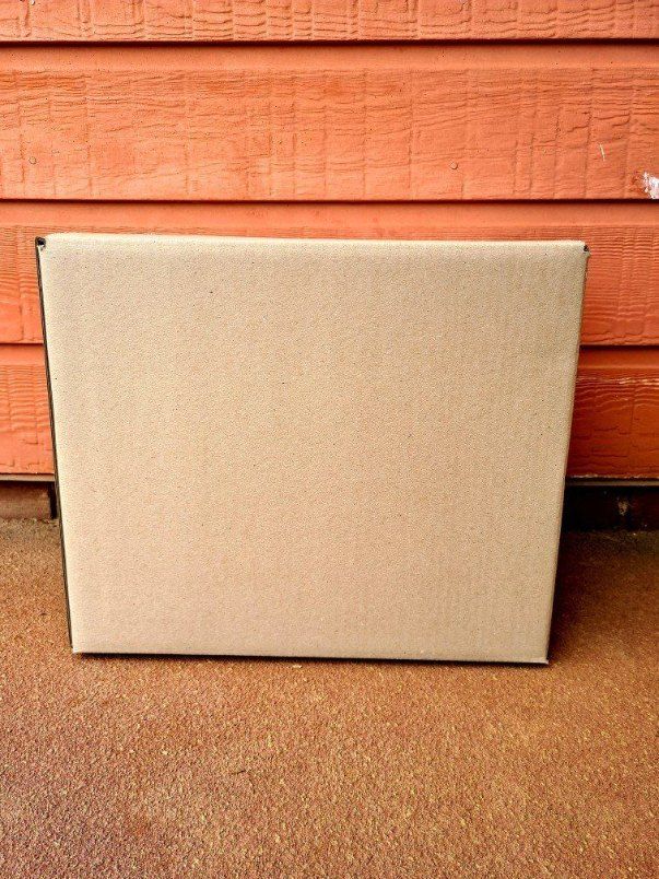 A Cardboard Box is Sitting on the Ground in Front of a Wooden Wall — Buck Removals & Storage in Cowra, NSW