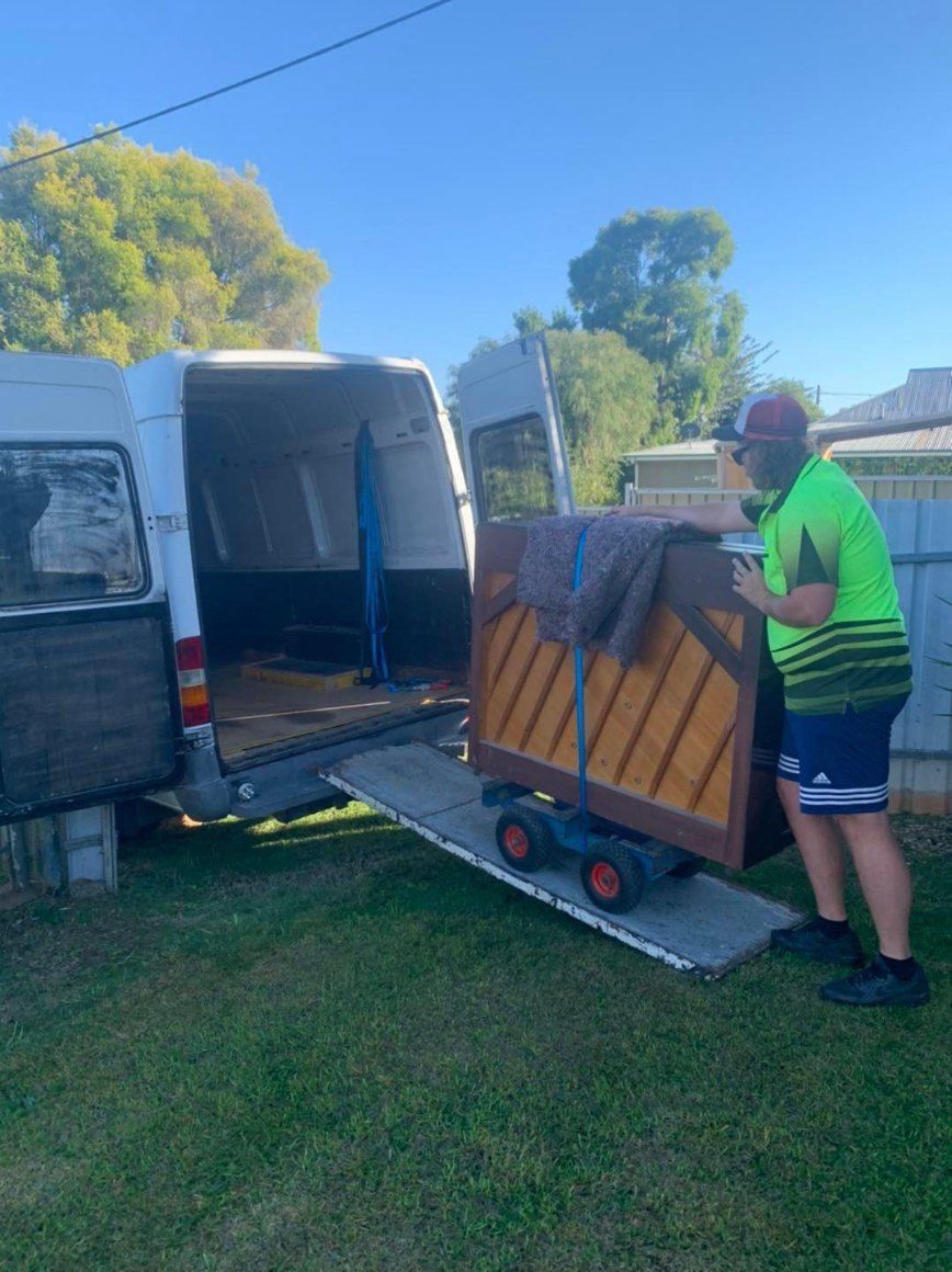 A Man is Pushing a Piano on a Dolly Out of a Van — Buck Removals & Storage in Cowra, NSW