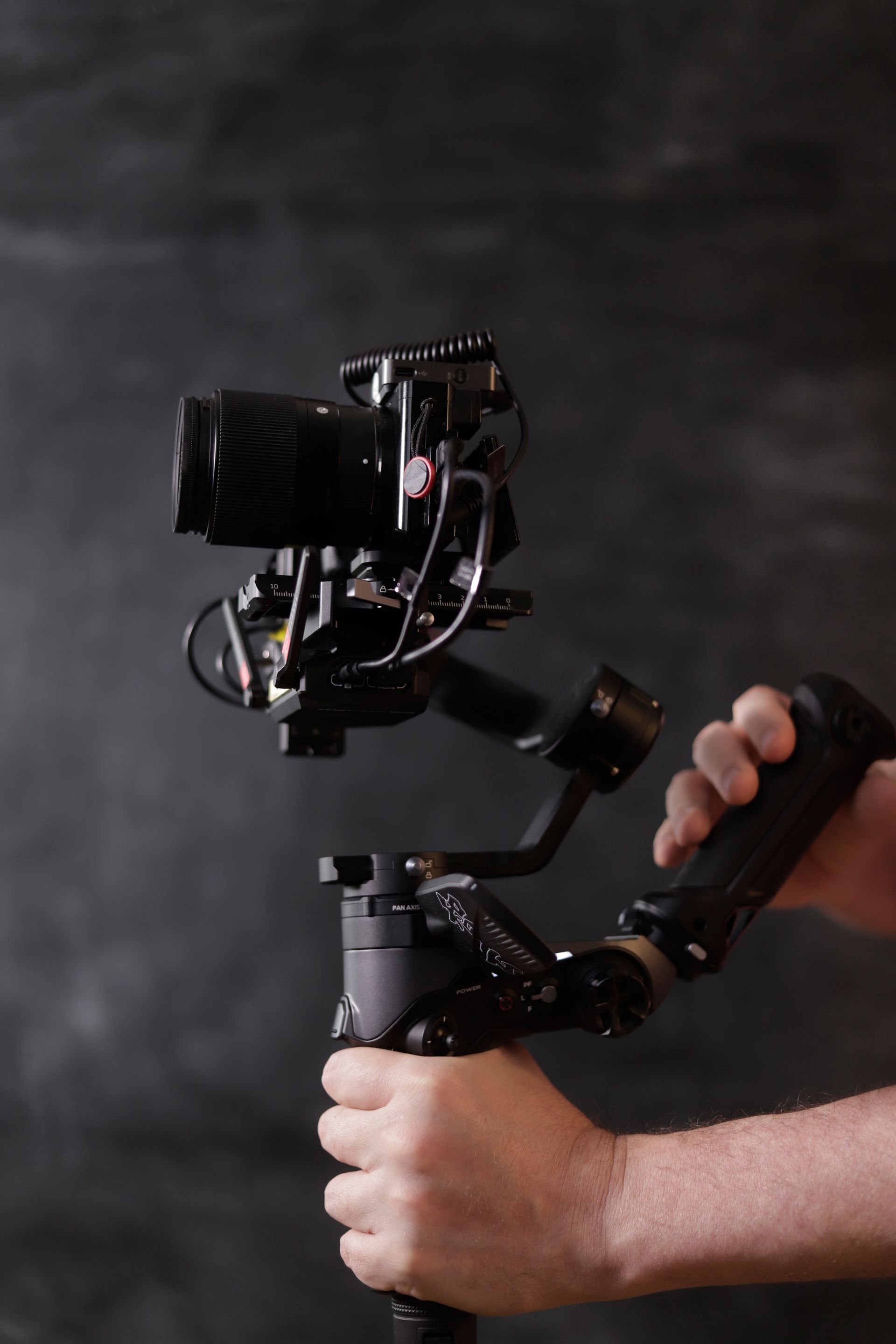 Persoon die een camera vasthoudt, gemonteerd op een cardanische ophanging, tegen een donkergrijze achtergrond.