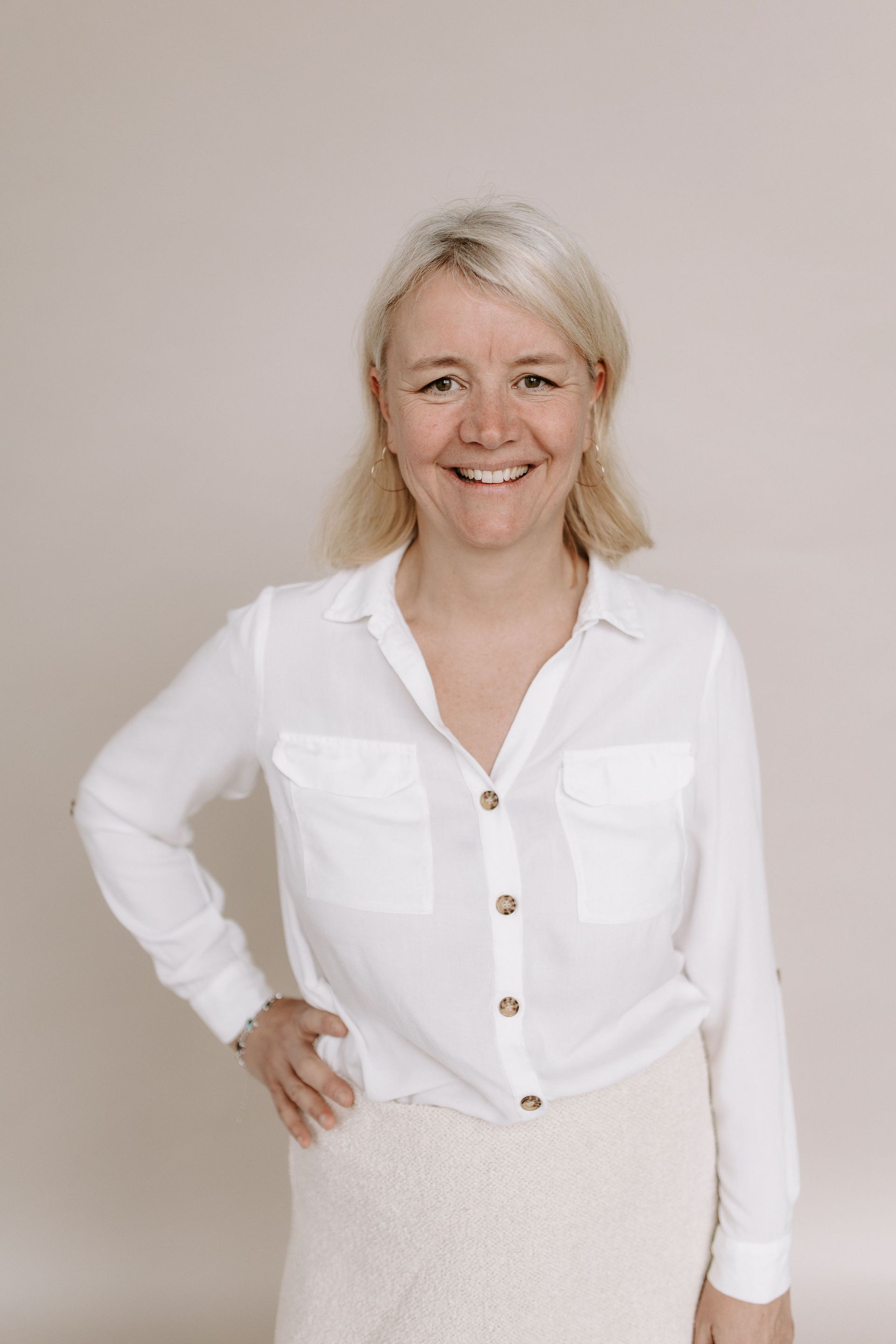Eine Frau trägt ein weißes Hemd und einen beigen Rock und lächelt.