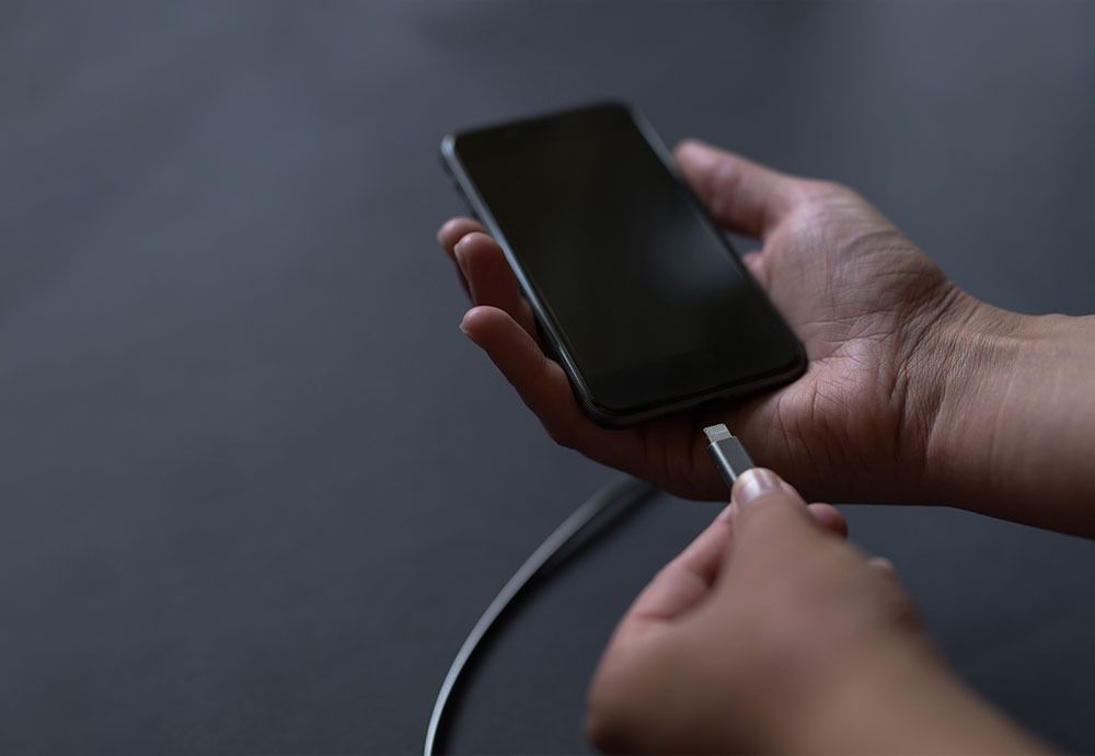 Hand Placing a Black Smartphone on a Charger — Phone Hut in Alice Springs, NT
