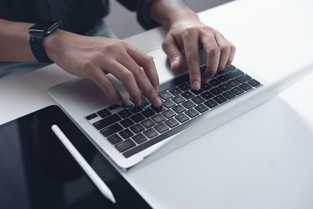 Person Typing on a Laptop Keyboard at a White Desk — Phone Hut in Alice Springs, NT