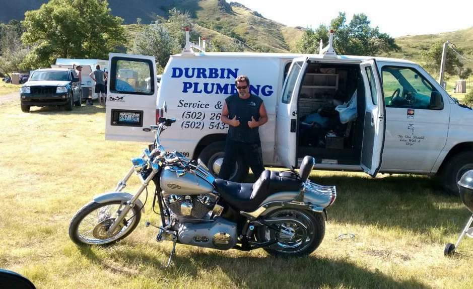 Plumber standing by white service van with motorcycles parked on grassy field outdoors