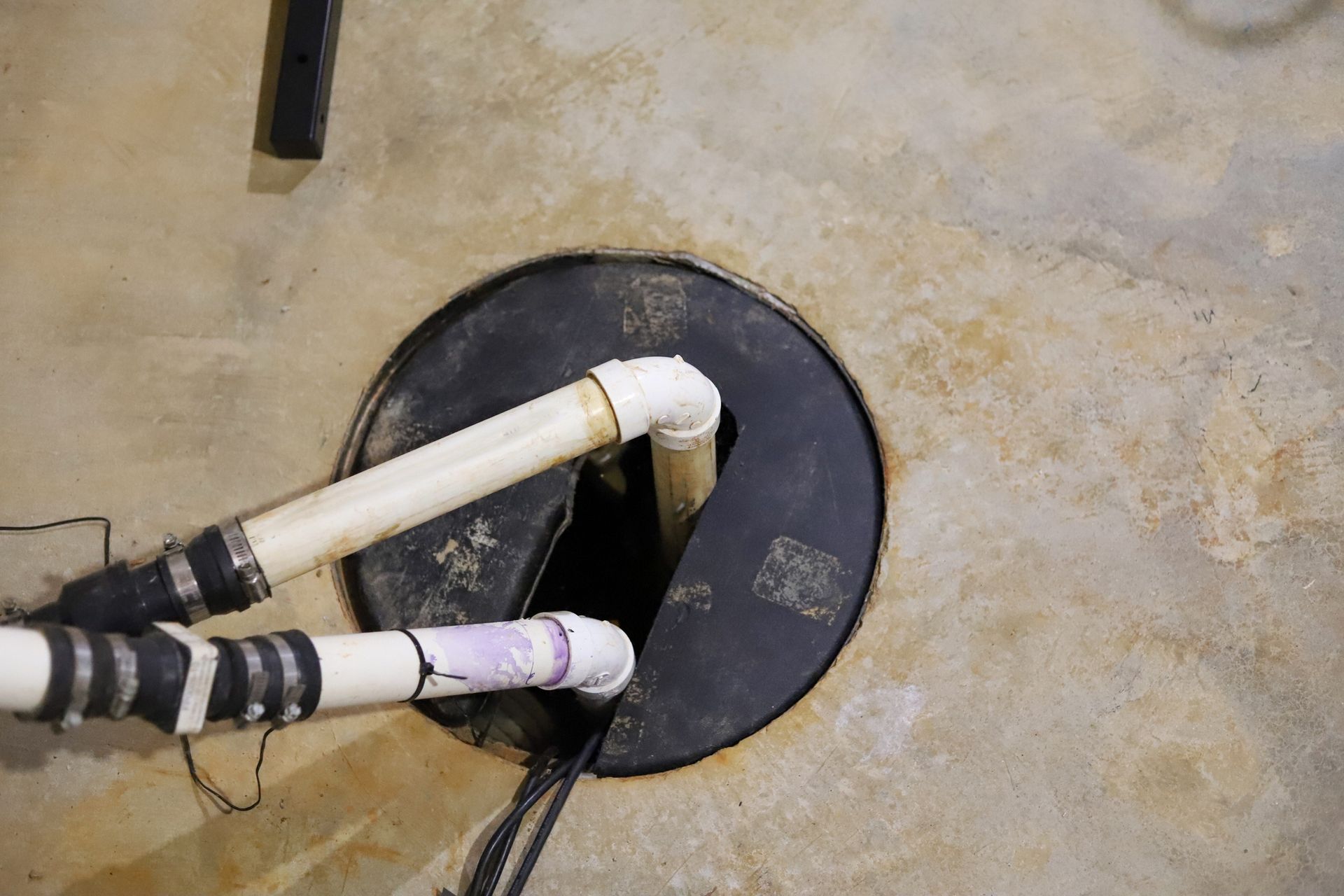 Two white pipes entering a black circular opening in a concrete floor