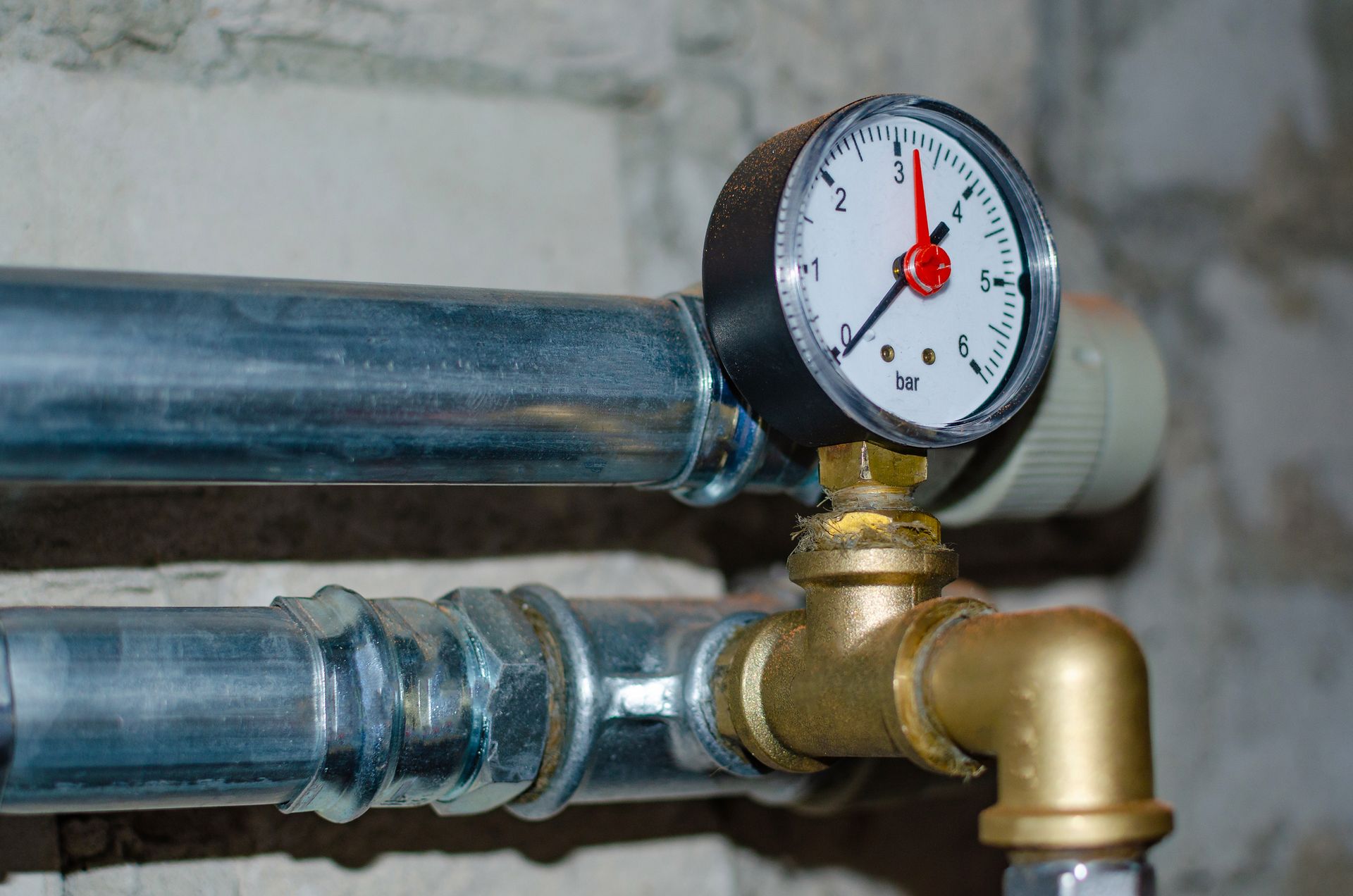 Pressure gauge on a brass pipe valve with blue insulated pipes in the background