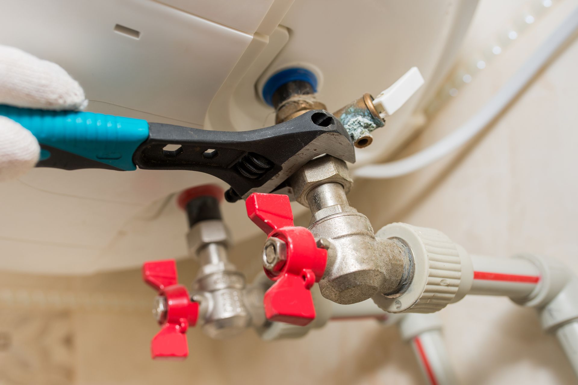 Plumber tightening a bathroom sink valve with pliers, showing red and silver water shutoff fixtures.