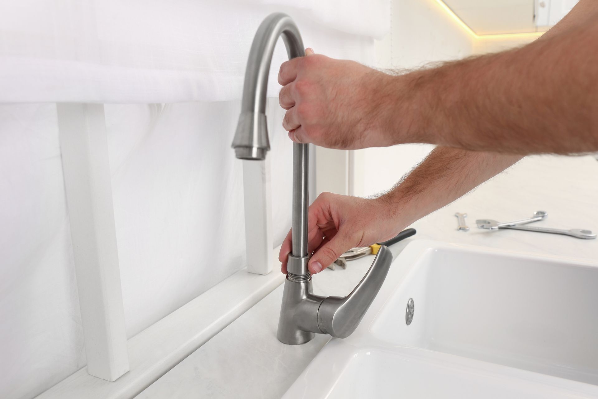 Hand holding a kitchen faucet handle over a stainless steel sink with pull-out sprayer
