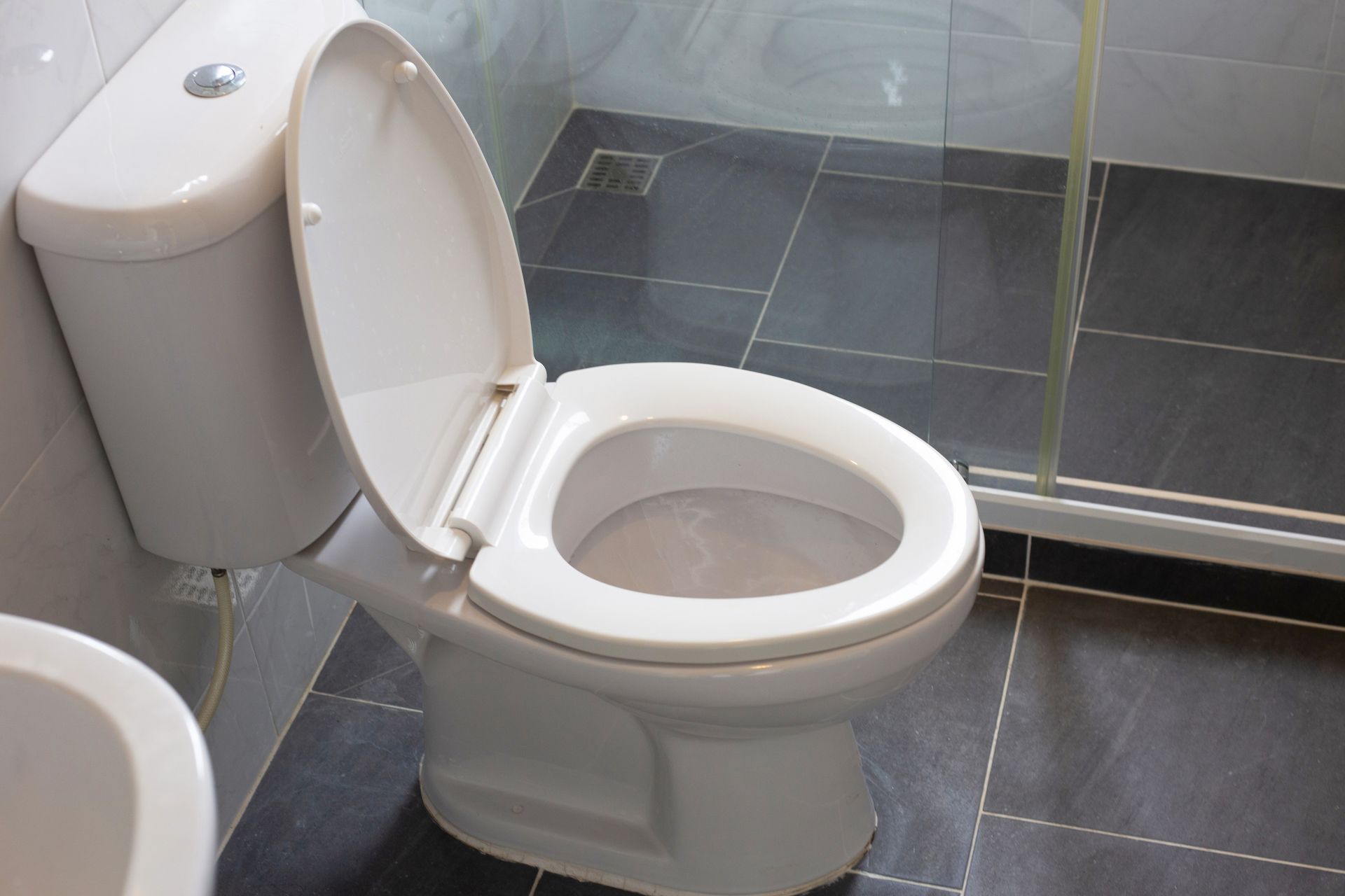 White toilet with lid open in a tiled bathroom beside a glass shower door.
