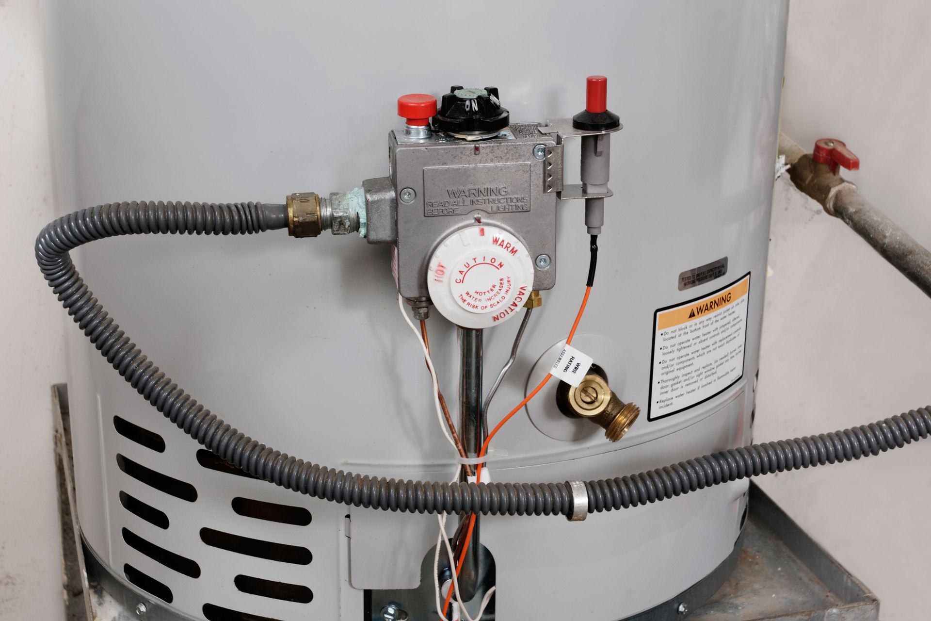 Gas water heater with connected pipes, valves, and flexible vent hose in a utility room